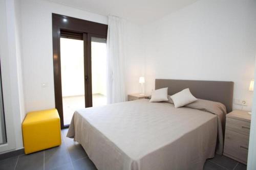 biała sypialnia z dużym łóżkiem i żółtym stołkiem w obiekcie Apartamentos Ocea w mieście Cambrils