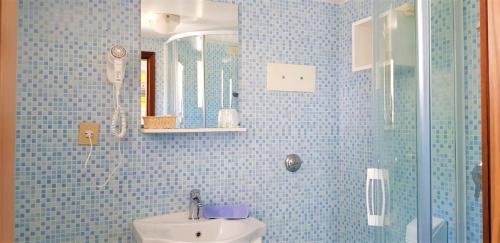 La salle de bains est pourvue de carrelage bleu, d'un lavabo et d'une douche. dans l'établissement Hotel Danubio, à Lido di Jesolo