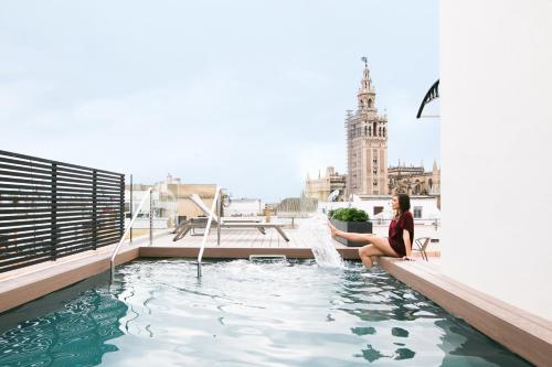 une femme assise sur le toit d'un immeuble avec piscine dans l'établissement Joya del Casco Boutique Hotel by Shiadu, à Séville