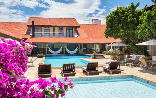 un complejo con piscina, sillas y flores púrpuras en Praia Hotel Imbituba, en Imbituba