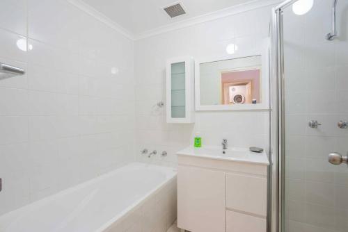 un bagno bianco con vasca e lavandino di Urban Escape – Strathfield a Sydney
