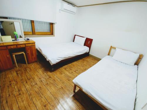 Habitación con 2 camas, escritorio y espejo. en Jeju Masil Guesthouse en Jeju
