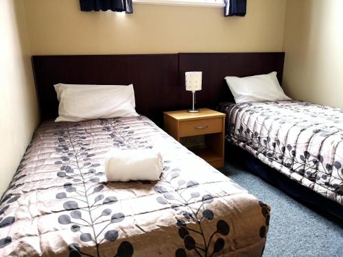 1 dormitorio con 2 camas y mesa con lámpara en 45 on Avenal Motel, en Invercargill