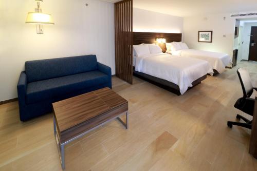 a hotel room with two beds and a blue couch at Holiday Inn Express & Suites - Playa del Carmen by IHG in Playa del Carmen