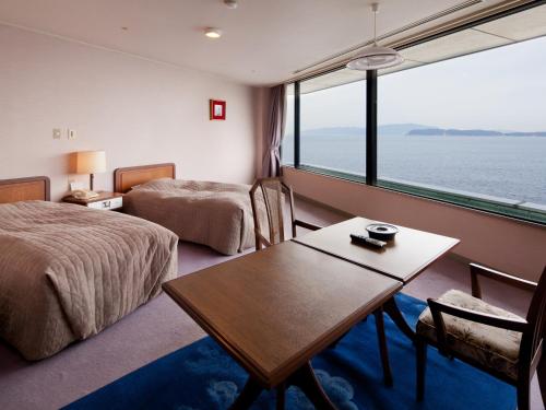 una camera d'albergo con due letti, un tavolo e una finestra di Wakayama Kada Onsen Kada Kaigetsu (ex. Azumaya Seaside Hotel) a Wakayama