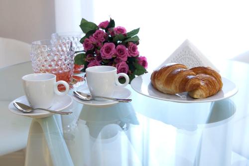 un tavolo con un piatto di croissant, tazze e fiori di Cardilli Luxury Rooms a Roma