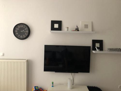 a flat screen tv on a white wall with a clock at Apartment Bjelasnica in Bjelašnica