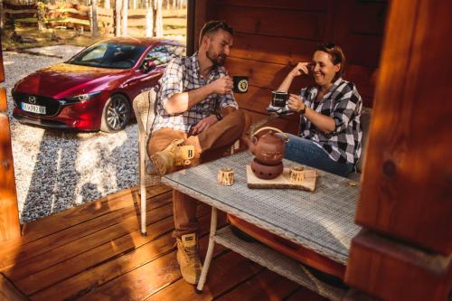 two men sitting on a porch with a table and a car at Łosia Chata in Grzybowce