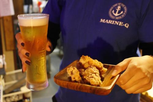 a man holding a plate of food and a glass of beer at MARINE-Q in Inami