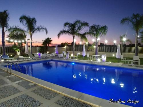 - une piscine avec des chaises et des palmiers la nuit dans l'établissement Villa Puccio, à Castelvetrano