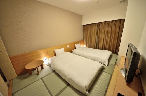 a small room with two beds and a television at Dormy Inn Hirosaki in Hirosaki