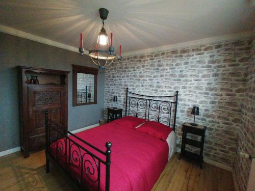 1 dormitorio con cama roja y pared de ladrillo en Les Chambres de KERCHELGEN, en Saint-Sauveur