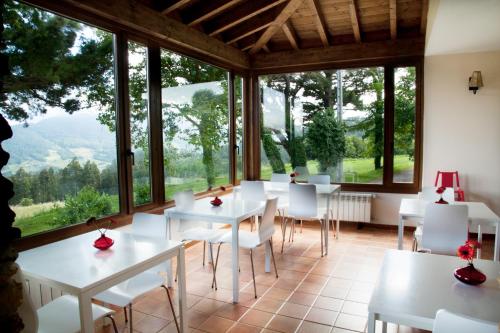 uma sala de jantar com mesas e cadeiras brancas e janelas grandes em La Casa de la Abuela Milagros em Pravia