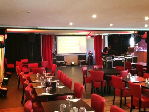 a dining room with tables and red chairs and a screen at Hôtellerie des jardins d'honvault in Wimereux