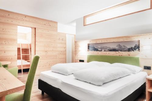 a bedroom with a white bed and a wooden wall at Kristiania Small Dolomites Hotel in Selva di Val Gardena