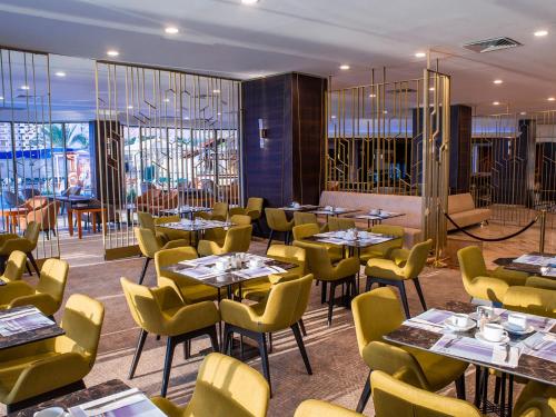 um restaurante com mesas, cadeiras amarelas e janelas em Caesar Premier Tiberias Hotel em Tiberíades