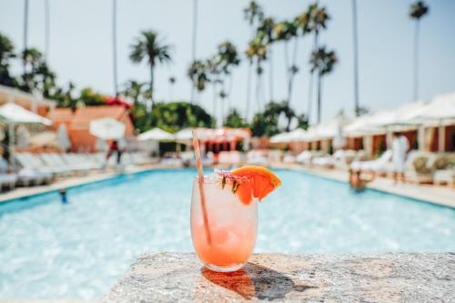 a drink sitting on a ledge next to a swimming pool at The Beverly Hills Hotel - Dorchester Collection in Los Angeles