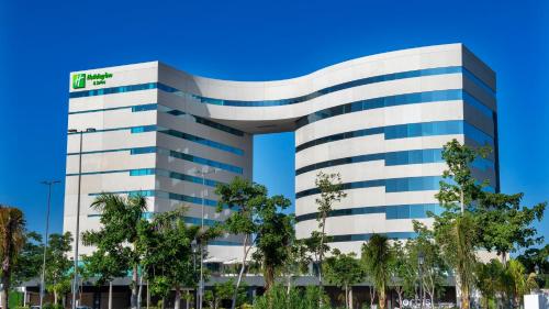a tall white building with trees in front of it at Holiday Inn & Suites - Merida La Isla by IHG in Mérida