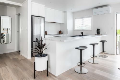 a white kitchen with a counter and stools at Awesome Beach House on Oceanview Road in Mount Maunganui