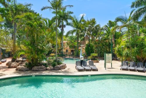 a swimming pool with two chairs and palm trees at Ashmore Palms Holiday Village in Gold Coast