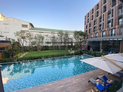 una piscina con sombrilla junto a un edificio en The Teak Hotel en Mae Sot