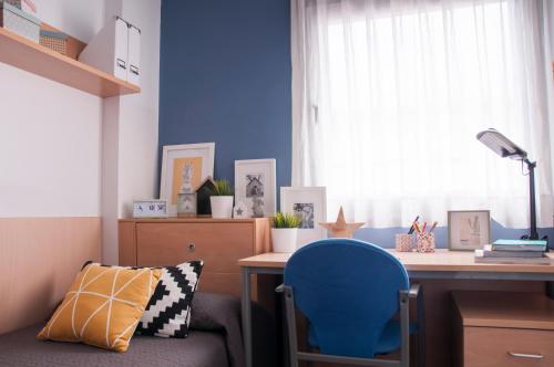 einen Schreibtisch mit einem blauen Stuhl in einem Zimmer mit einem Fenster in der Unterkunft Residencia Tomás Alfaro Fournier in Vitoria-Gasteiz