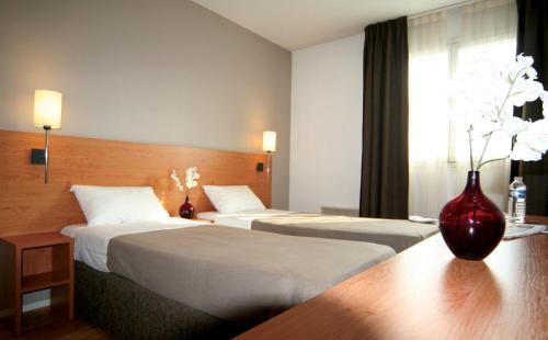 オルレアンにあるセジュール ＆ アフェール オルレアン ジャンヌ ダルクのベッド2台、テーブルの上に花瓶が備わるホテルルームです。