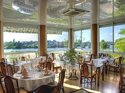 a dining room with tables and chairs and large windows at Le Grand Monarque in La Charité-sur-Loire