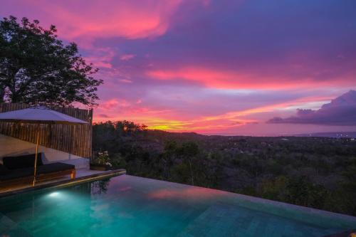 a swimming pool with a sunset in the background at OCEANNA - Uluwatu, Bali in Uluwatu