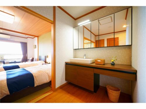 a bedroom with a bed and a sink and a mirror at Tenku Yubo Seikaiso in Beppu