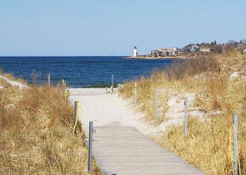 a wooden path leading to a beach with a lighthouse at Elegant Gloucester Beach Getaway with Ocean Views! in Gloucester