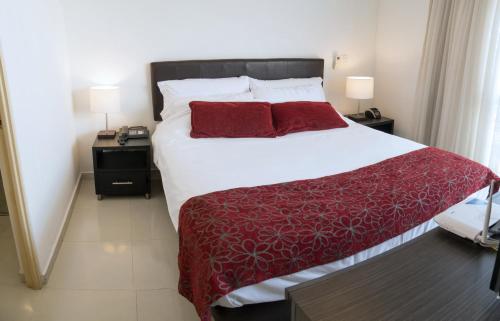 Confortable y Tranquilo Aparta Suite en el Corazón de Bucaramanga, Exterior con hermosa vista sobre la ciudad في بوكارامانغا: غرفة نوم بسرير أبيض كبير مع شراشف حمراء