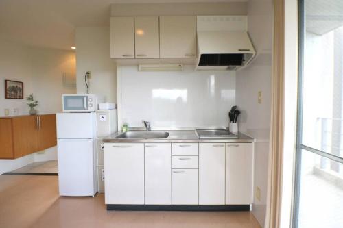 a white kitchen with a sink and a refrigerator at 読谷村カービラハウス ow3 in Jima