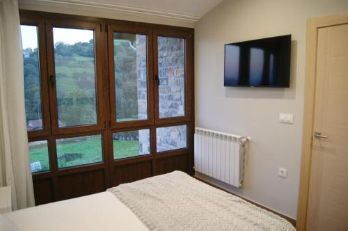 1 dormitorio con 1 cama, TV y ventana en Apartamentos Rurales Peñon Blanco, en Peñerudes