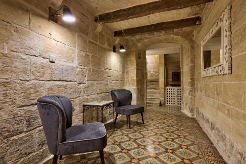 two chairs and a table in a room with a stone wall at Barrakka Suites in Valletta