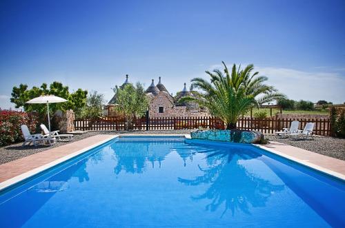 a blue swimming pool with two chairs and a house at Trulli Il Castagno in Martina Franca