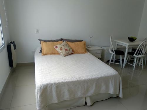 Un dormitorio con una cama blanca con almohadas y una mesa en La Suitte en Bahía Blanca