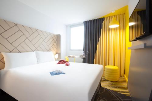 パリにあるイビス スタイル パリ マセナ オリンピアードの白いベッドと黄色の壁が備わるホテルルームです。