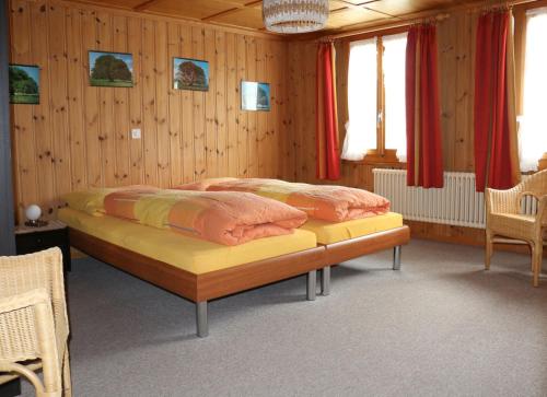 2 camas en una habitación con paredes de madera y cortinas rojas en Bühlerhof, en Lenk