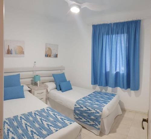 Habitación con 2 camas y cortina azul en Apartamentos Delfines, en Cala Blanca