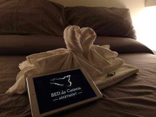 カターニアにあるBED.da Catania Apartmentの毛布を敷いたベッドの上に座る看板