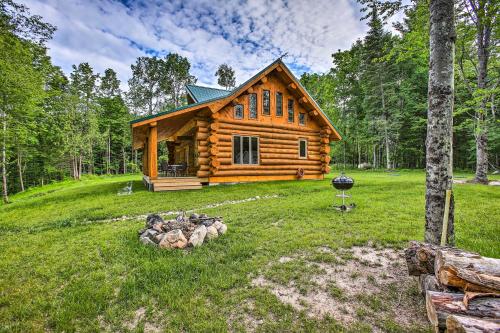 a log cabin in the woods with a pile of logs at Custom Log Cabin with Deck and 45 Acres By Pine River! in Tustin