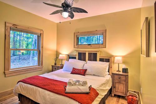 a bedroom with a bed with a ceiling fan and two windows at Romantic Asheville Area Cabin with Deck and Hot Tub! in Leicester