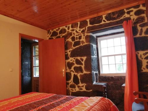 a bedroom with a stone wall with a bed and a window at Casa da Alícia in Feiteira