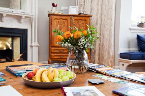 a table with a bowl of fruit and a vase of flowers at Abbey Manor Luxury Guesthouse in Cape Town