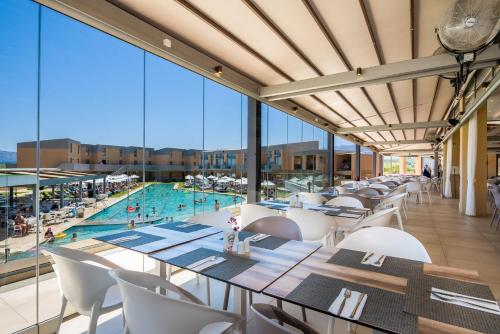 a restaurant with a pool and tables and chairs at Kiani Beach Resort Family All Inclusive in Kalyves