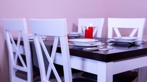 a dining room table with white chairs and a candle at Wesoła Apartamenty in Wólka Kosowska