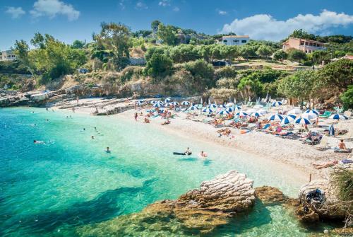 a beach with people and umbrellas in the water at Melina Oasis Boutique Hotel in Kassiopi