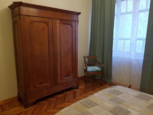 a bedroom with a wooden cabinet and a chair next to a window at Appartamento Rosalba in Asti