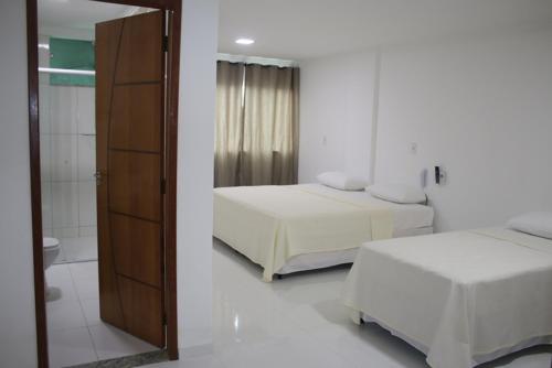 a white room with two beds and a mirror at Hotel Vista Bela in Itamaraju